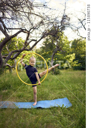 little 5-year-old gymnast in a black minimalistic leotard exercises with a hoop in the garden 115890738