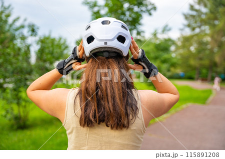 Portrait of roller skater woman putting on helmet in inline skates before rollerblading in park. Outdoor activities. Summer roller skating. Portrait of roller skater woman putting on helmet in inline skates before rollerblading in park. Outdoor activities. Summer roller skating. 115891208