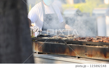 Chef prepares meat on grill in open air 115892148
