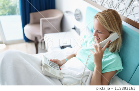 Woman on bed talking on phone in hotel room 115892163