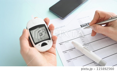 Patient holding glucometer and recording data in diary closeup 115892560