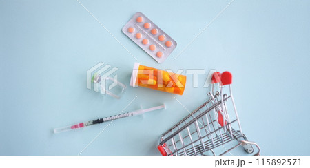 Many medicines and syringe lying near toy metal basket closeup 115892571