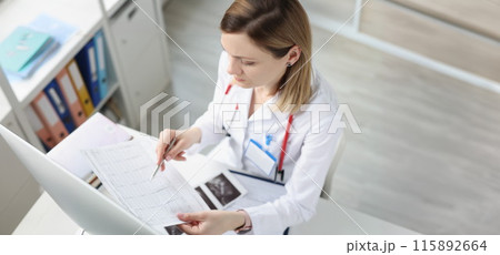 Doctor sitting at table and looking at cardiogram in clinic Doctor sitting at table and looking at cardiogram in clinic 115892664