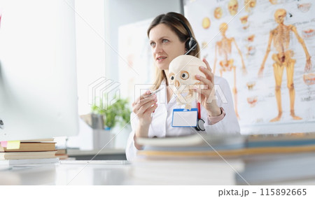 Doctor in headphone with microphone showing skull in computer screen Doctor in headphone with microphone showing skull in computer screen 115892665