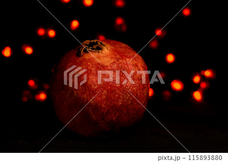 pomegranate fruit close up on a black background with glowing lights in the background 115893880
