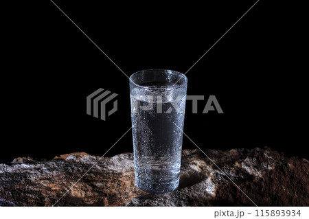 a glass of water with walls fogged up from the cold on a rock on a black background a glass of water with walls fogged up from the cold on a rock on a black background 115893934