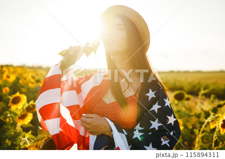 Beautiful girl in hat with the American flag in a sunflower field. 4th of July. Fourth of July. Freedom 115894311
