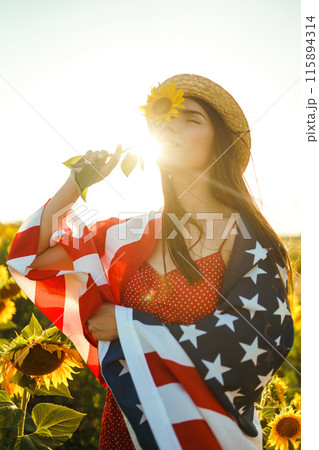 Beautiful girl in hat with the American flag in a sunflower field. 4th of July. Fourth of July. Freedom 115894314