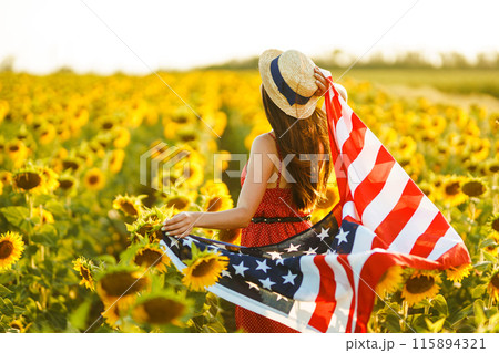 Beautiful girl in hat with the American flag in a sunflower field. 4th of July. Fourth of July. Freedom 115894321