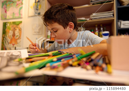 Kids have art class, drawing, painting with teacher in workshop. A young boy is engaged in drawing with colored pencils in a creative studio environment. 115894480