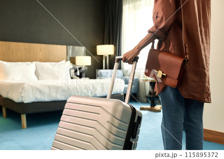 Cropped back view of African American woman entering hotel room and holding suitcase copy space 115895372