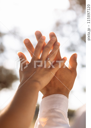 Close up loving couple hold hands showing engagement ring with diamond on ring finger on nature background. Newly married groom in white shirt and bride express their feeling. Wedding, Valentines day Close up loving couple hold hands showing engagement ring with diamond on ring finger on nature background. Newly married groom in white shirt and bride express their feeling. Wedding, Valentines day 115897120
