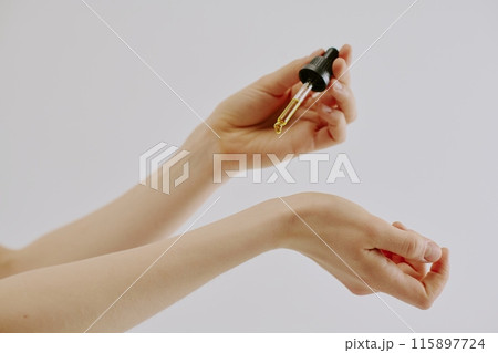 Womans manicured hand holding glass pipette full of golden aromatic essence and dripping it Womans manicured hand holding glass pipette full of golden aromatic essence and dripping it 115897724