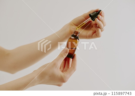 Female hands holding brown glass bottle and glass pipette full of organic golden essence Female hands holding brown glass bottle and glass pipette full of organic golden essence 115897743