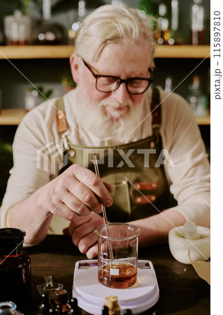 Mature perfumer blending finished perfume and smiling lightly and tiredly in home perfume lab 115897810