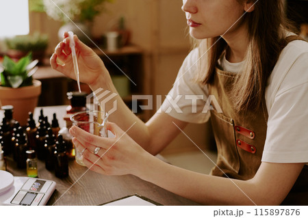 Medium close up of female perfumer adding new essential oil while she preparing new perfume for selling Medium close up of female perfumer adding new essential oil while she preparing new perfume for selling 115897876