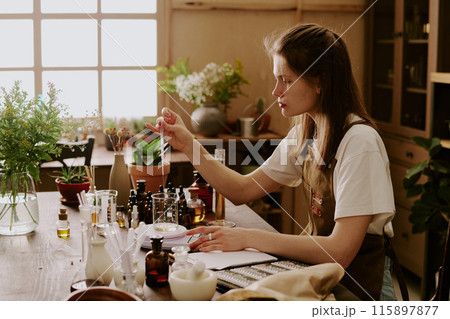 Young perfumer weighing glass flask with organic essence and adding new essential oil Young perfumer weighing glass flask with organic essence and adding new essential oil 115897877