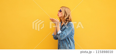 Beautiful stylish young woman blowing kiss in glasses, denim jacket posing on yellow wall background Beautiful stylish young woman blowing kiss in glasses, denim jacket posing on yellow wall background 115898010