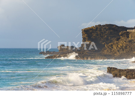 A blurry image of a beach with waves crashing on rocks under the sky 115898777