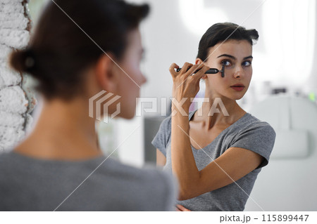 A young woman massages her face with gouache while looking in the mirror. 115899447