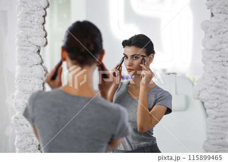 A young woman massages her face with gouache while looking in the mirror. 115899465