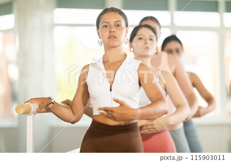 Young ballerinas stand in second position near ballet barre during group training in dance studio 115903011