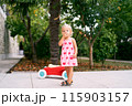 Little girl stands near a toy car on a paved path in the garden. High quality photo 115903157