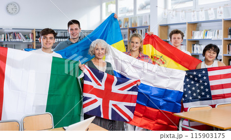 Portrait of positive teenagers and female teacher with flags of different countries in school library 115903175