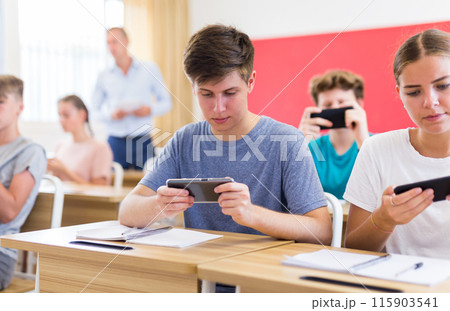 Young students with smartphones sitting in class room Young students with smartphones sitting in class room 115903541