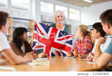 Elderly teacher shows the flag of Great Britain to teenagers and talks about this country during lesson at library school Elderly teacher shows the flag of Great Britain to teenagers and talks about this country during lesson at library school 115903802