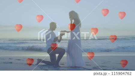 Image of red heart balloons floating over couple in love man proposing a woman with a ring on beach 115904762