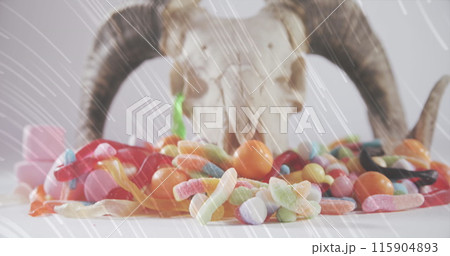Light trails over halloween candies and goat horns and skull against white background 115904893
