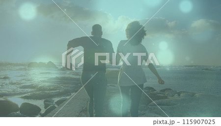 Image of spots of light over african american couple running on the rocks near the sea 115907025