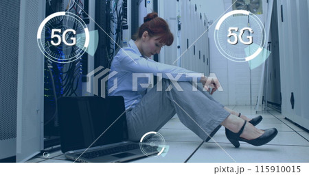 Digital composite of a Caucasian woman sitting beside a laptop in a corridor of server towers while Digital composite of a Caucasian woman sitting beside a laptop in a corridor of server towers while 115910015