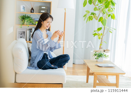 リビングでくつろぎながらスマホを見る若い女性 115911444