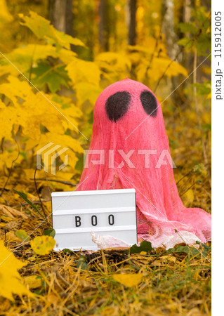 Creative handmade Halloween holiday decoration. pink ghost with Lightbox BOO text in autumn leaves forest. Zero waste homemade decor. Mystic place 115912005