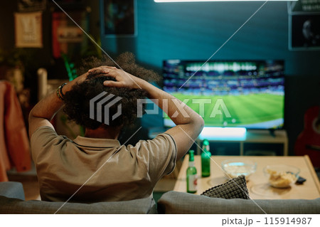 Back view of disappointed unrecognizable man watching soccer match on TV in living room at home, copy space Back view of disappointed unrecognizable man watching soccer match on TV in living room at home, copy space 115914987