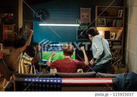 Rear view of ethnically diverse male friends spending evening in living room watching soccer match on TV, copy space 115915037