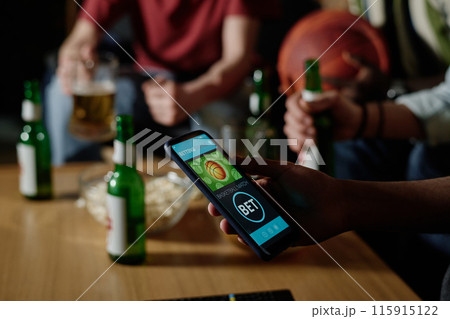 Unrecognizable man holding smartphone betting on favorite team while watching basketball game with his friends in evening Unrecognizable man holding smartphone betting on favorite team while watching basketball game with his friends in evening 115915122