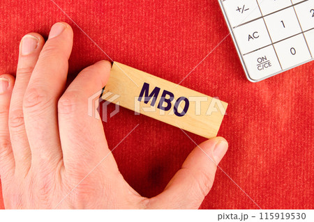 Management by Objectives MBO written on wooden blocks with a hand, part of a calculator on a red background 115919530