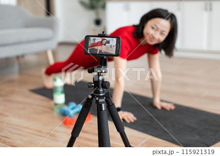 Woman recording herself doing push-ups at home Woman recording herself doing push-ups at home 115921319