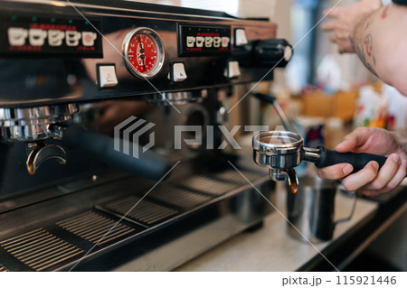 Close-up hands of unrecognizable barista male preparing tasty coffee drink, holding equipment of coffee maker coffee portafilter filled with finely ground coffee. Beverage drink for breakfast in cafe. Close-up hands of unrecognizable barista male preparing tasty coffee drink, holding equipment of coffee maker coffee portafilter filled with finely ground coffee. Beverage drink for breakfast in cafe. 115921446