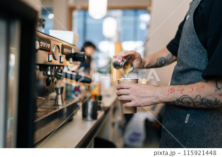 Cropped shot of unrecognizable barista male preparing tasty coffee drink for customer in small business, holding metal pot pouring coffee in espresso shot. Beverage drink for breakfast in cafe. Cropped shot of unrecognizable barista male preparing tasty coffee drink for customer in small business, holding metal pot pouring coffee in espresso shot. Beverage drink for breakfast in cafe. 115921448