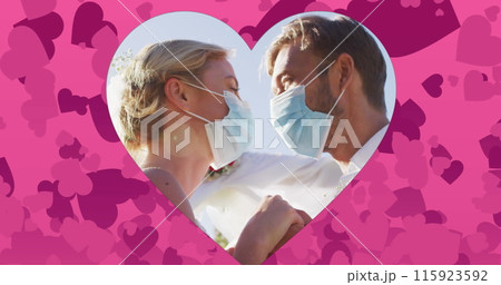 Image of hearts over married caucasian couple with face masks 115923592