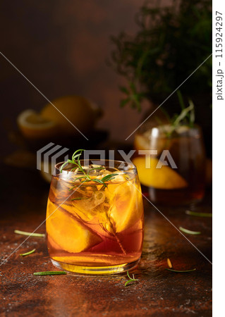 Iced tea or cocktail with ice, rosemary and lemon slices on the old brown table. Iced tea or cocktail with ice, rosemary and lemon slices on the old brown table. 115924297
