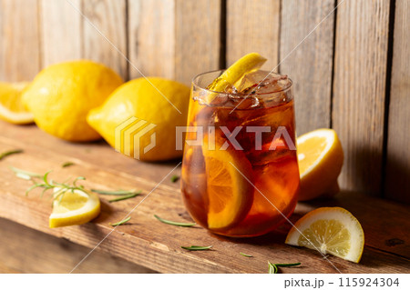 Iced tea or alcoholic cocktail with ice, rosemary and lemon slices on a old wooden table. Iced tea or alcoholic cocktail with ice, rosemary and lemon slices on a old wooden table. 115924304