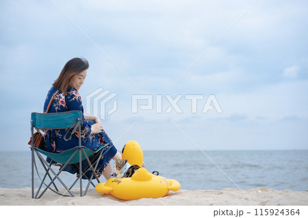 woman relax and sit on beach chair with her cat sit on duck rubber ring on sand beach woman relax and sit on beach chair with her cat sit on duck rubber ring on sand beach 115924364