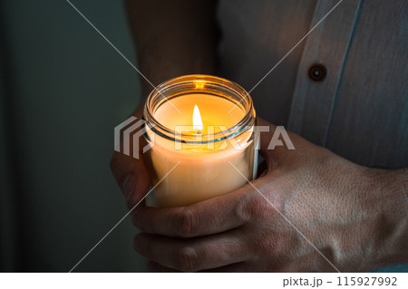 Man holding a burning candle in his hands, elegant young man with candle jar, meditation and mindfulness concept Man holding a burning candle in his hands, elegant young man with candle jar, meditation and mindfulness concept 115927992