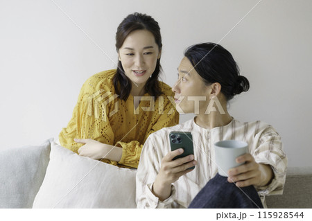 リビングのソファに座ってスマホを見るミドルエイジの男性と後ろからスマホを覗くミドルエイジの女性 リビングのソファに座ってスマホを見るミドルエイジの男性と後ろからスマホを覗くミドルエイジの女性 115928544