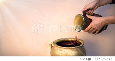 A hand holds a clay jar and pours water A hand holds a clay jar and pours water 115929251